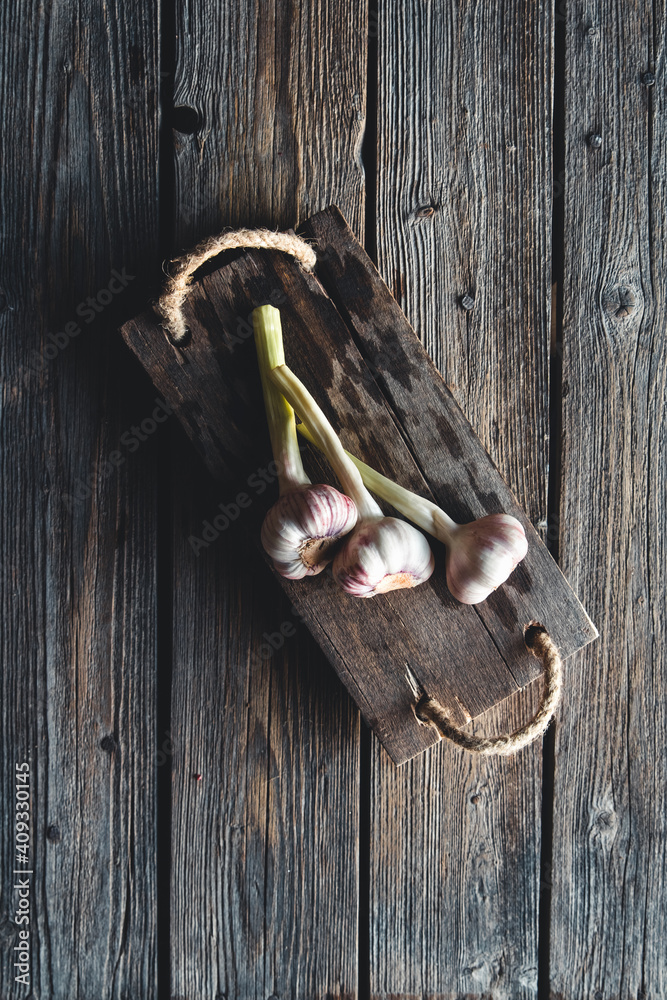 Fresh garlic heads in wooden bord on old dark wooden background