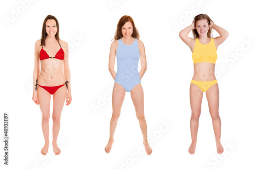 Full length portraits of three gorgeous laughing women wearing colorful swimwear, isolated in front of white studio background