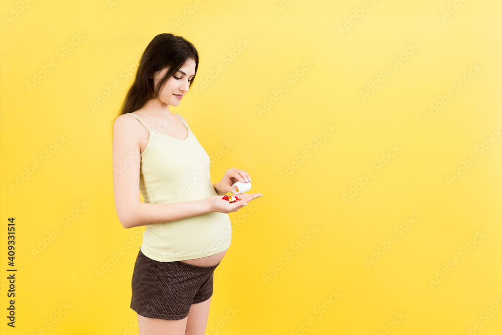 pregnant woman taking a pile of pills from a bottle at colorful background with copy space. Health care during pregnancy concept pregnant woman taking a pile of pills from a bottle at colorful background with copy space. Health care during pregnancy concept