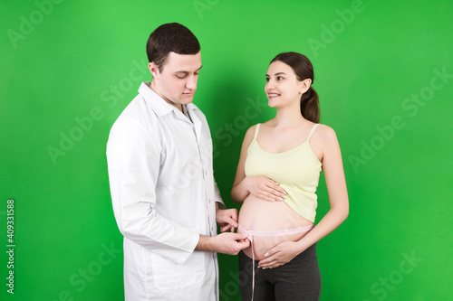 happy beautiful pregnant young woman touching her bare tummy while a doctor is measuring it photo