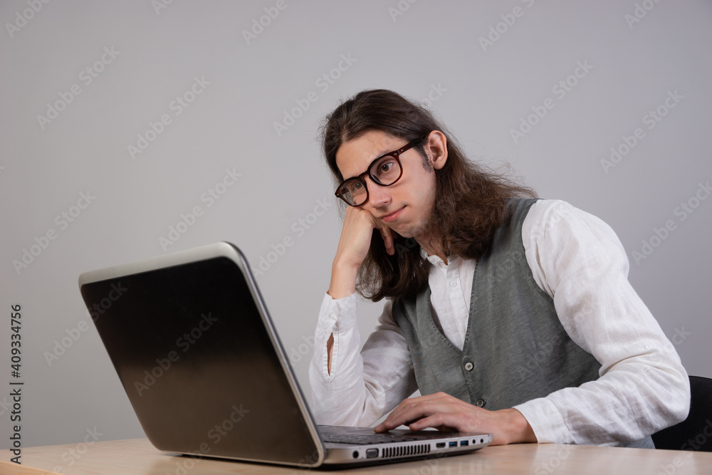 bored student is sitting at a laptop. Guy is a geek gamer, uses a laptop. Uninteresting course