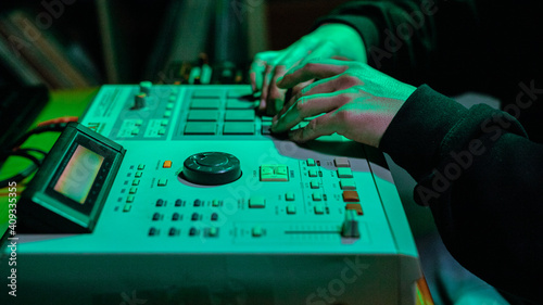 The hands of an artist creating music with his drum machines under green light.