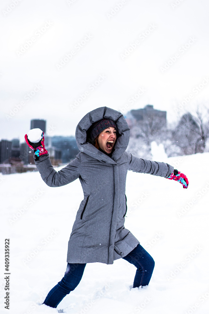 Beautiful active young woman having a snowball fight in Montreal, she is happy and screaming, city in background
