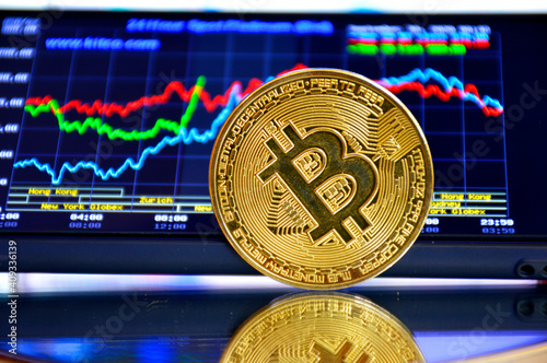 gold coin bitcoin stands edge on glass against the background of the stock chart