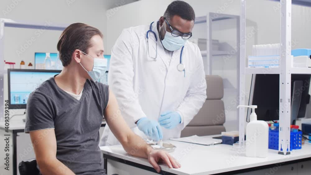 African-American doctor makes a coronavirus vaccine using a syringe and hypodermic needle. Medical worker and patient at the hospital office. Vaccination and safety concept. African-American doctor makes a coronavirus vaccine using a syringe and hypodermic needle. Medical worker and patient at the hospital office. Vaccination and safety concept.