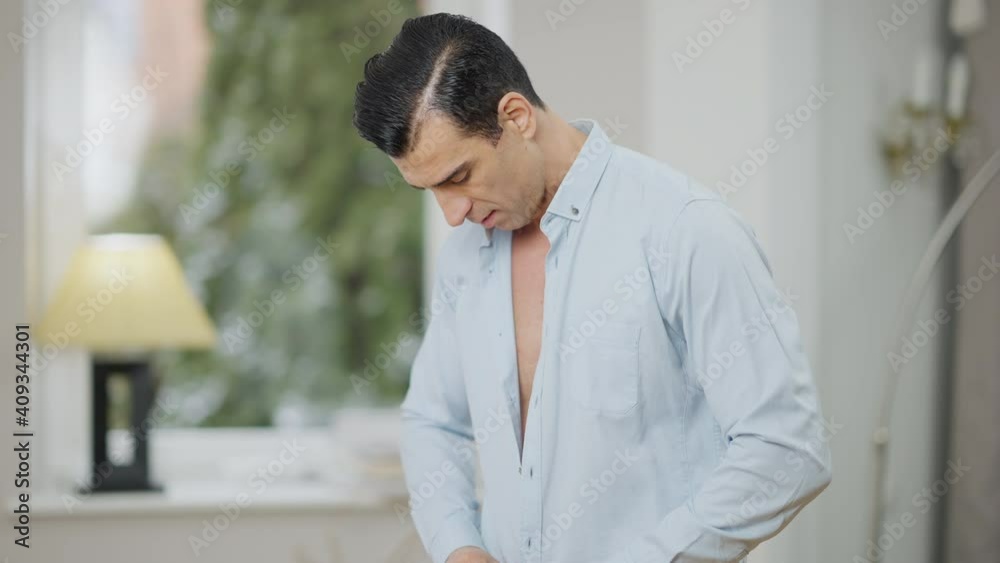 Confident young Middle Eastern man buttoning shirt in slow motion. Portrait of handsome stylish tattooed guy dressing up at home in the morning. Style and lifestyle concept. Confident young Middle Eastern man buttoning shirt in slow motion. Portrait of handsome stylish tattooed guy dressing up at home in the morning. Style and lifestyle concept.