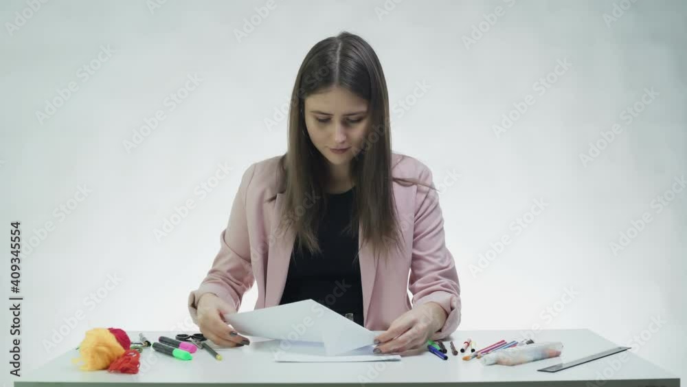Attractive young woman makes a paper plane at the table in a white studio Attractive young woman makes a paper plane at the table in a white studio