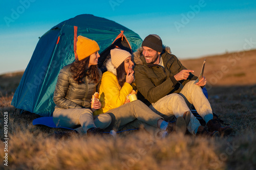 A Group of smiling friends sit and enjoy a mountain sunset looking at a map next to their tent.