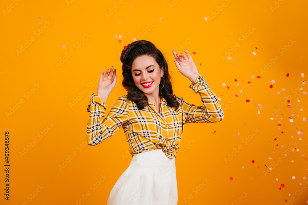 Excited pinup girl dancing and waving hands. Studio shot of blissful dark-haired woman in checkered shirt. Excited pinup girl dancing and waving hands. Studio shot of blissful dark-haired woman in checkered shirt.
