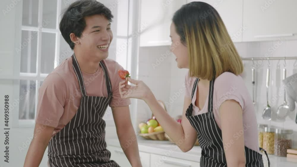 Happy Asian beautiful young family couple husband and wife enjoying smile and laugh, woman hold the strawberry to the man's nose spending time together in kitchen at home. Slow motion Happy Asian beautiful young family couple husband and wife enjoying smile and laugh, woman hold the strawberry to the man's nose spending time together in kitchen at home. Slow motion