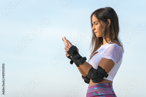 Beautiful young woman texting outdoors in the park in front of the ocean with roller blades equipment