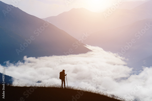 Silhouette of a man traveler in the mountains early in the morning at sunrise. The valley is filled with clouds