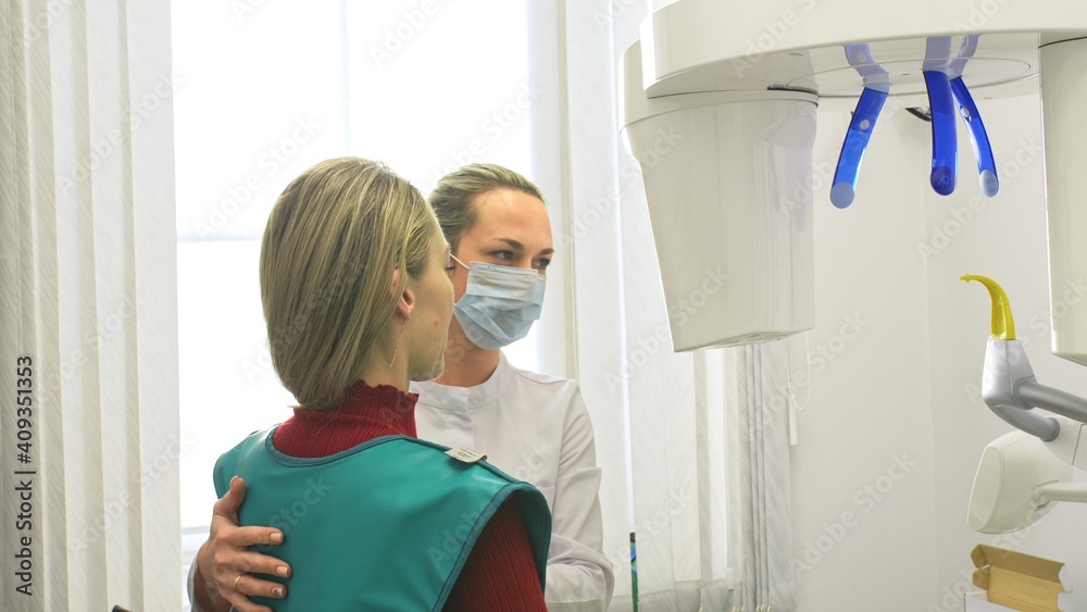 Doctor to take a image 3d scanner tomography of teeth and jaw in modern laboratory dental clinic. Female nurse shows the patient woman an x-ray machine 3d digital scanner. Computer dental diagnostics. Doctor to take a image 3d scanner tomography of teeth and jaw in modern laboratory dental clinic. Female nurse shows the patient woman an x-ray machine 3d digital scanner. Computer dental diagnostics.