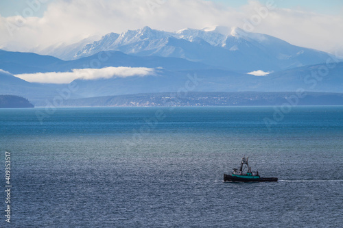 A fishing boat in Puget sound sailing in front of the Olympic Mountains in the distance.