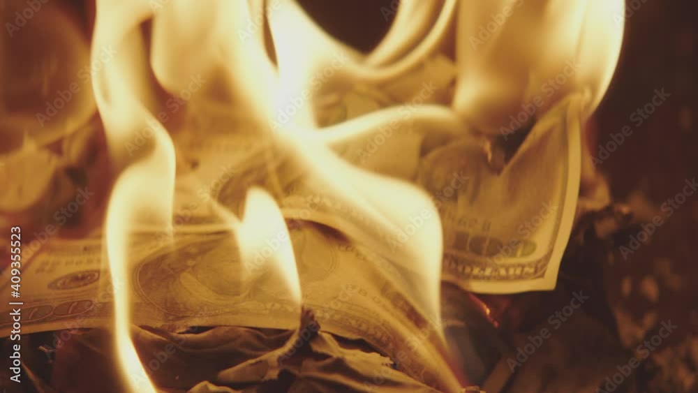 A pile of one hundred dollar bills are engulfed in flames and slowly burn. A pile of one hundred dollar bills are engulfed in flames and slowly burn.