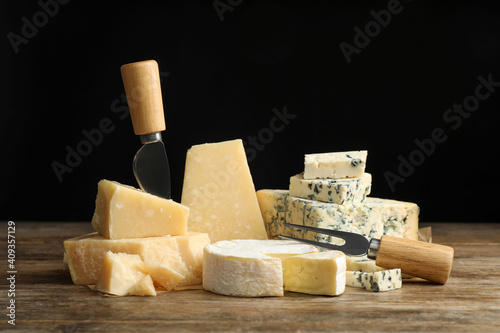 Different sorts of cheese, fork and knife on wooden table against black background