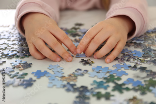 Little child playing with puzzles at table, closeup