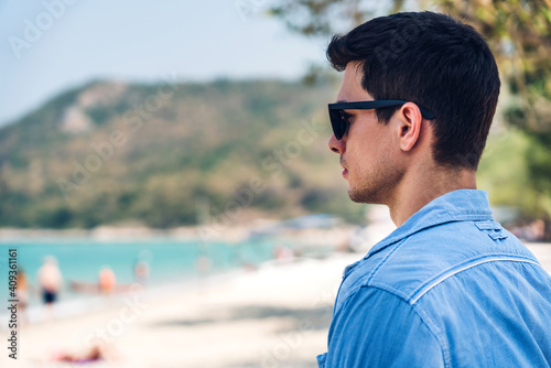 Portrait of smiling happy handsome man model enjoying and relax in fashionable hipster summer sunglasses standing on the tropical beach and looking at sea.Summer vacations and travel