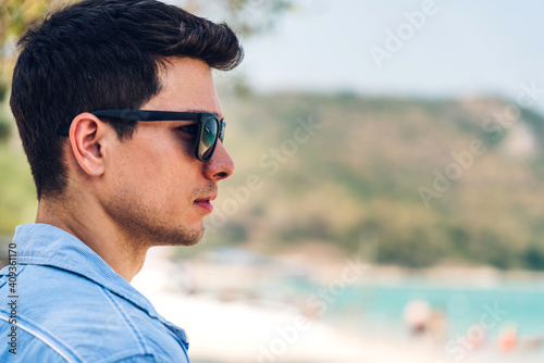 Portrait of smiling happy handsome man model enjoying and relax in fashionable hipster summer sunglasses standing on the tropical beach and looking at sea.Summer vacations and travel