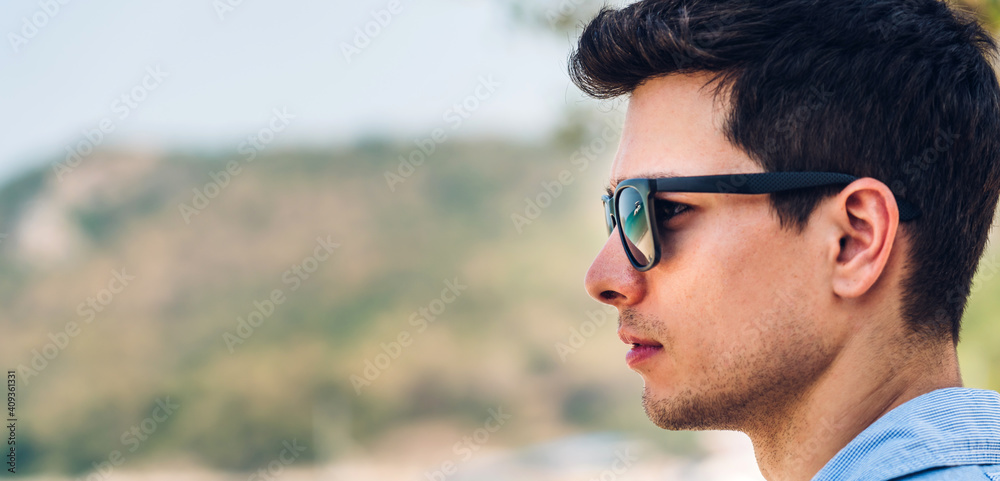 Portrait of smiling happy handsome man model enjoying and relax in fashionable hipster summer sunglasses standing with copy space banner for adding text on the tropical beach and looking at sea.Summer Portrait of smiling happy handsome man model enjoying and relax in fashionable hipster summer sunglasses standing with copy space banner for adding text on the tropical beach and looking at sea.Summer