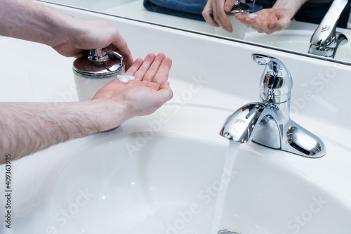 Washing your hands with hot soap and water to prevent disease and illness. Hands pressing a soap dispenser and cleaning hands under bathroom sink tap background