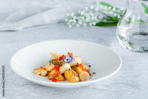 Scallops, potatoes, red caviar, fresh flowers decor in round plate
