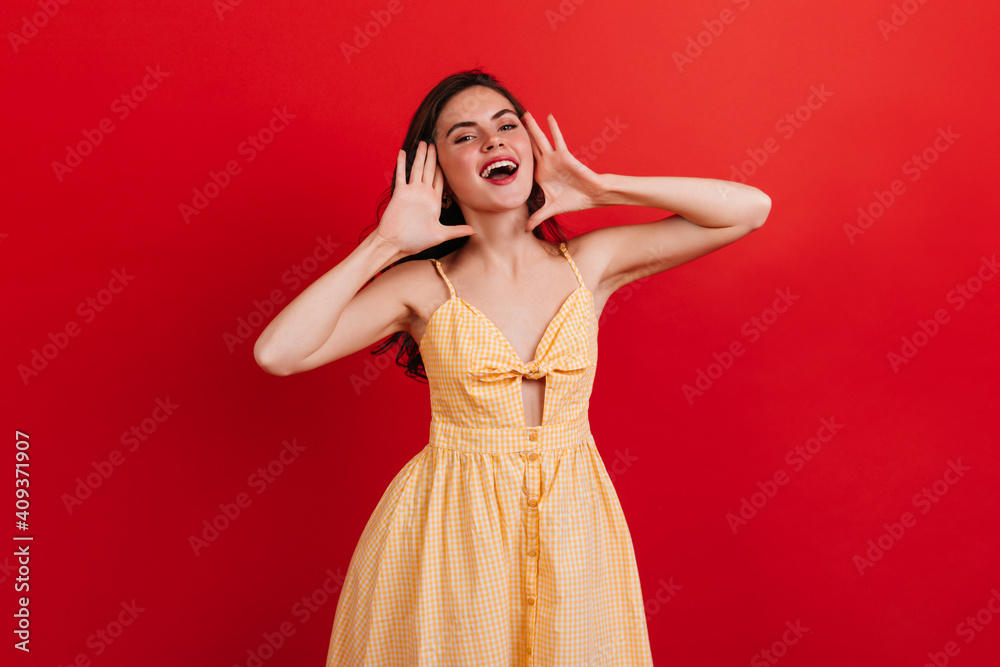Pretty girl in great mood screams loudly. Portrait of lady with red lipstick in checkered sundress on isolated bright background