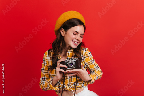 Active lady is cute smiling on red background. Brunette woman takes photo on retro camera