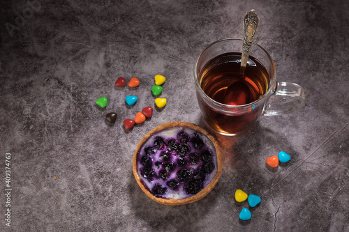 Tea in a glass cup with a spoon, blueberry cake and candy on a gray background