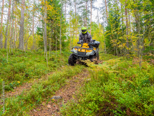 ATV rider rides among tall grass. He travels on quad cycle. ATV rider stands still while riding. ATV rider rides in a yellow helmet. He travels through green forest. Extreme tourism by quad cycle