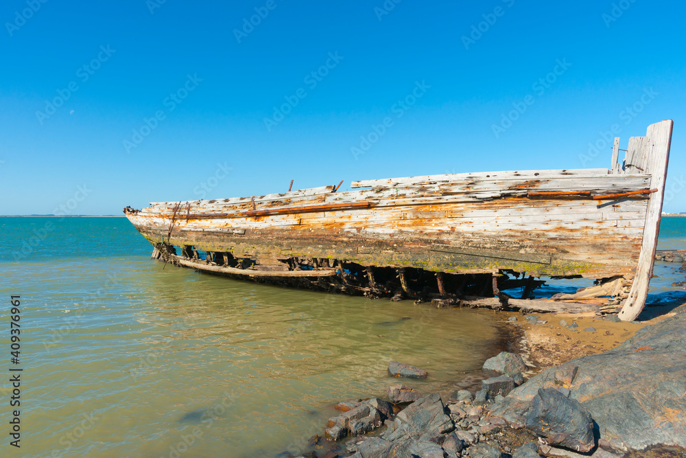 Rotting holed hulk of old wooden fishing boat beached