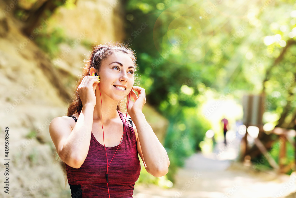 Young contented woman in sportswear in the park listens to music on headphones while exercising on the street. Healthy lifestyle concept