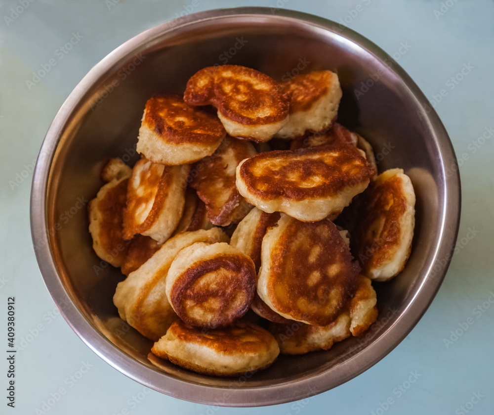 Fried dough pancakes close up in a metal dish on a blue background of the table Fried dough pancakes close up in a metal dish on a blue background of the table