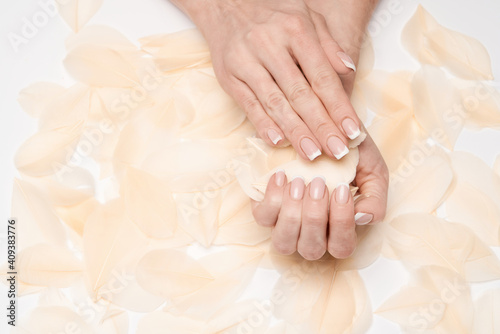 Beautiful Female Hands with French manicure and feathers over light grey background