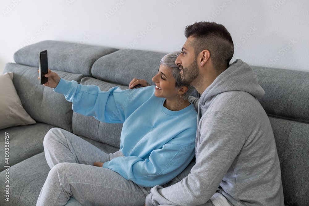 Beautiful young loving couple bonding to each other and making selfie while sitting on the couch together Beautiful young loving couple bonding to each other and making selfie while sitting on the couch together