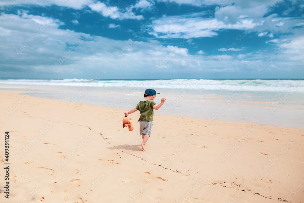 Baby running on the beach with a bear on his hand. Baby running on the beach with a bear on his hand.
