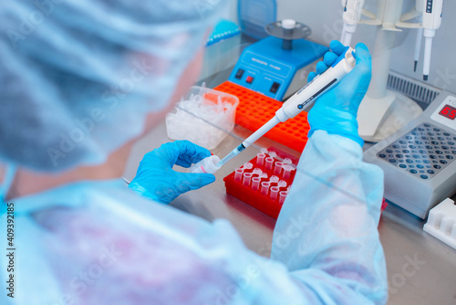 Dna test in the lab. a laboratory technician with a dispenser in his hands is conducting dna analysis in a sterile laboratory behind glass photo