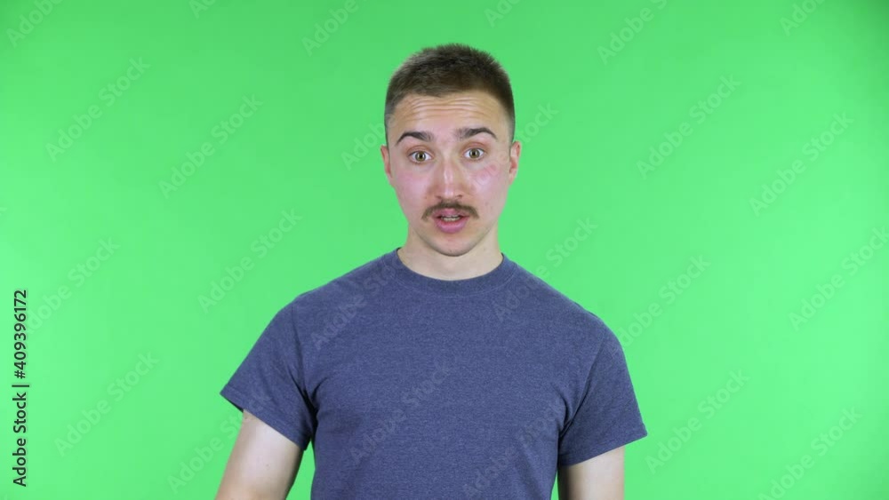 Portrait of a young man looking at camera, scolding and shaking her index finger. Cute male with a mustache in a blue t-shirt posing on a green screen in the studio. Close up. Portrait of a young man looking at camera, scolding and shaking her index finger. Cute male with a mustache in a blue t-shirt posing on a green screen in the studio. Close up.