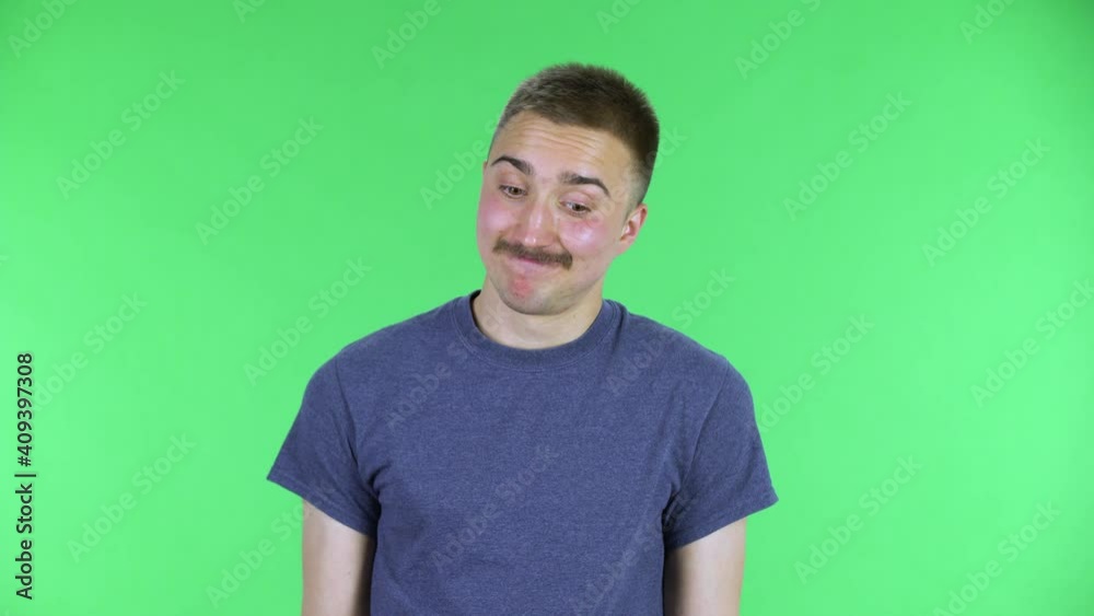 Portrait of a young man looking at the camera shrugging, sighing and shakes his head. Cute male with a mustache in a blue t-shirt posing on a green screen in the studio. Close up. Portrait of a young man looking at the camera shrugging, sighing and shakes his head. Cute male with a mustache in a blue t-shirt posing on a green screen in the studio. Close up.