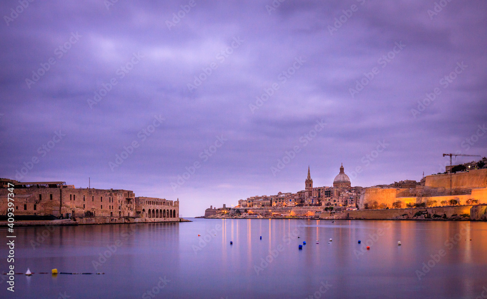 sunset on the city of valletta, malta with purple cloudy sky and ancient buildings in the background