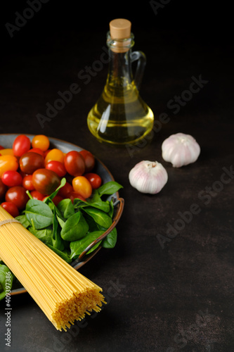 Low key photo of raw spaghetti with spinach, tomato, garlic and olive oil