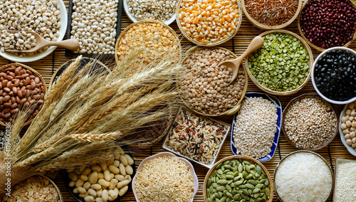 Variety kind of dry organic cereal and grain seeds in wooden and ceramic bowl with bundle of dry wheat in dark tone, for healthy or clean food ingredient or agricultural product concept