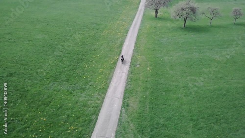 Aerial shot of motoryclist riding adventure motorbike on a dirt road in the countryside in Switzerland. Concept of freedom. Drone aerial shot.