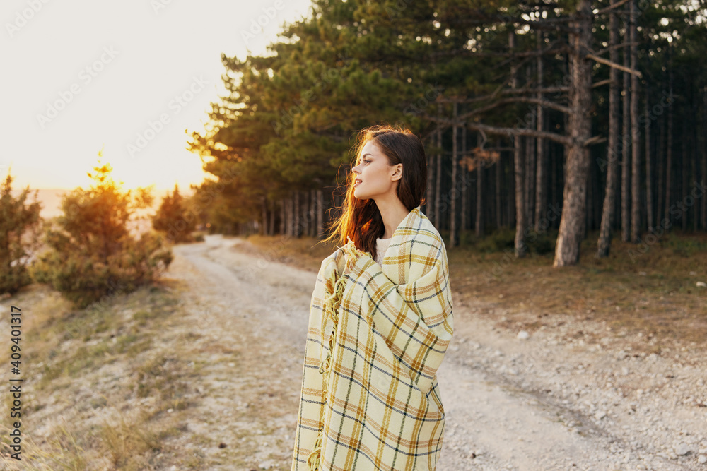 Beautiful woman with a warm blanket near the road and a coniferous forest in the background