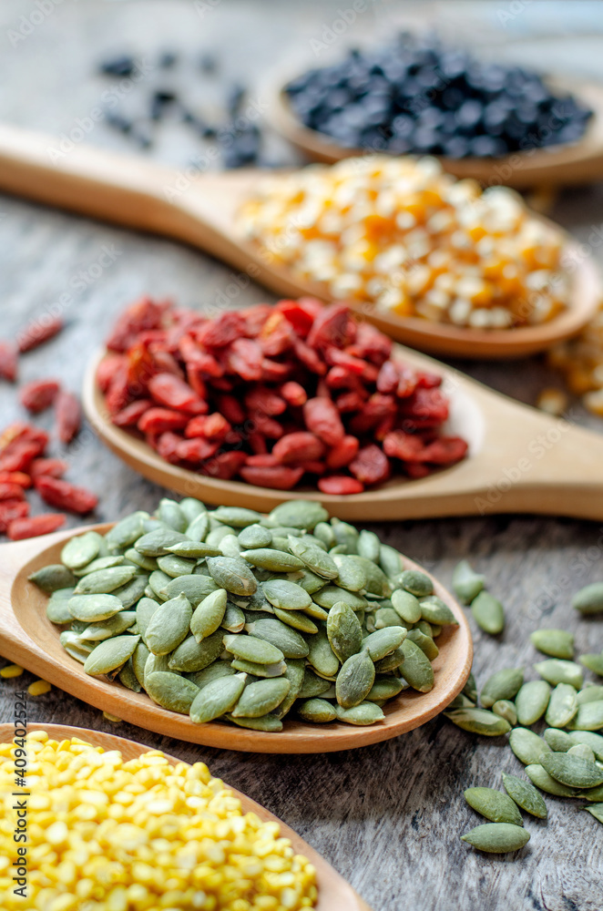 Fototapeta premium Closed up dry green pumpkin seeds in wooden spoon with blur goji berry, corn, black bean and mung on grunge background