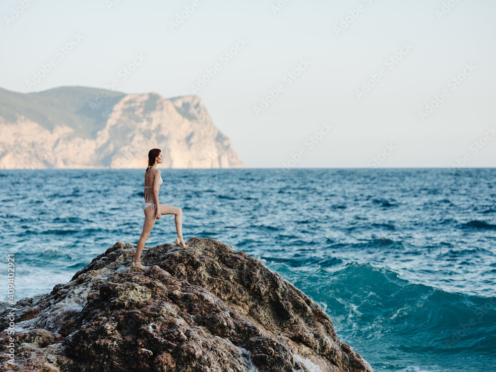 woman stands on a high rock in nature near the sea and a mountain in the backgroun