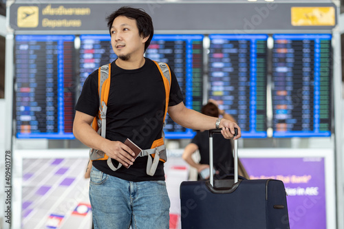 Portrait of Asian traveler with luggage with passport standing over the flight board for check-in at the flight information screen in modern an airport, travel and transportation concept. photo