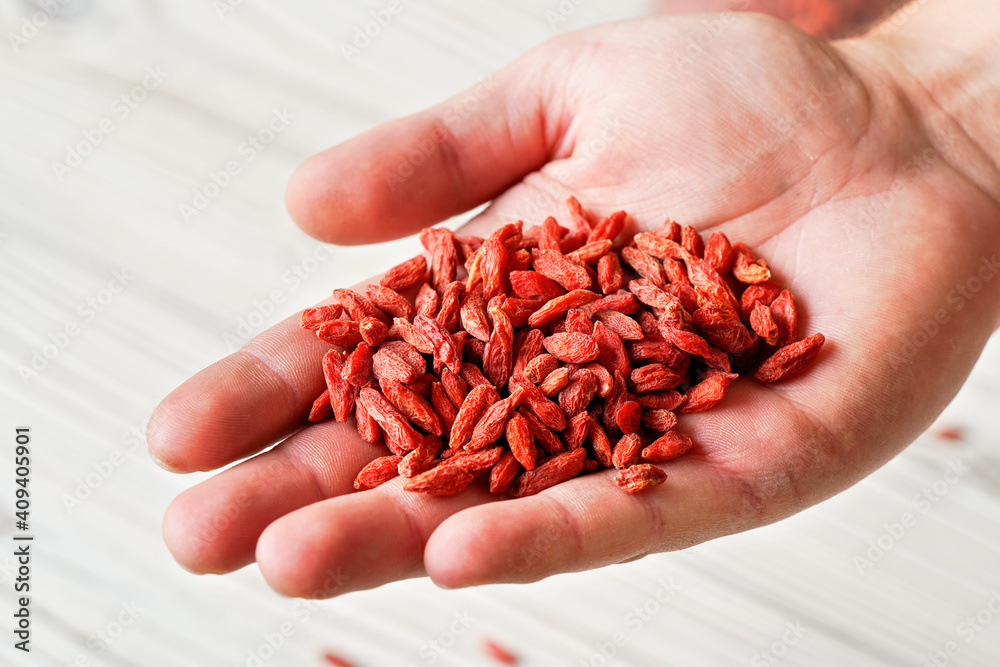 © Lubo Ivanko - Young man hand with dried goji berries over white boards desk, closeup detail