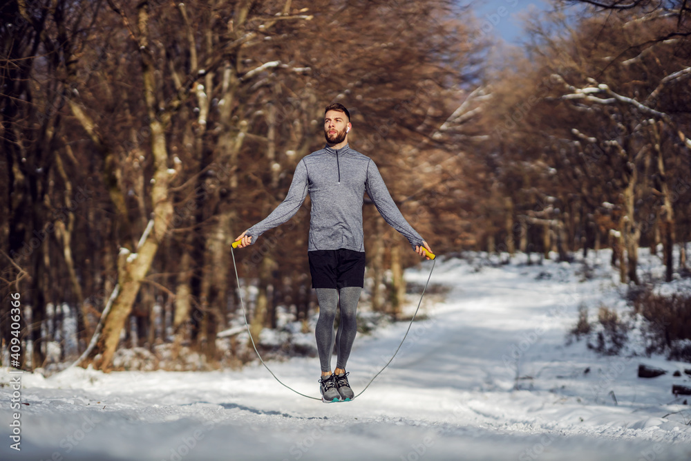 Fit sportsman jumping the rope in forest at snowy winter day. Healthy life, winter fitness, sportswear