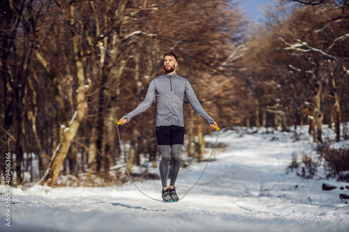 Fit sportsman jumping the rope in forest at snowy winter day. Healthy life, winter fitness, sportswear